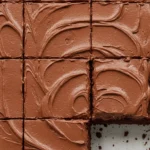 Voici un gâteau au chocolat au lait crémeux, coupé en parts individuelles et disposé sur une plaque à pâtisserie. Un morceau a été retiré, révélant le papier sulfurisé en dessous.