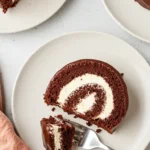 Vue aérienne de trois assiettes contenant des parts de gateau roule au chocolat, nappé d'un glaçage brillant et fourré de crème blanche, avec une fourchette sur l'assiette centrale, invitant à déguster ce dessert gourmand.