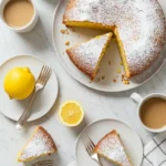 Gâteau au citron recette facile : Vue de dessus d'un délicieux gâteau saupoudré de sucre glace, servi avec du café et des citrons frais.