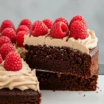 Un délicieux Gâteau Chocolat Sans Farine, nappé d'une crème légère et garni de framboises fraîches, dont une part est en train d'être coupée.