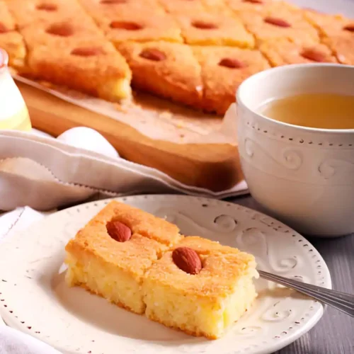 Dégustation d'un gateau arabe : Deux parts de gateau arabe, décorées d'amandes, sont présentées sur une assiette, accompagnées d'une tasse de thé, pour une expérience culinaire authentique