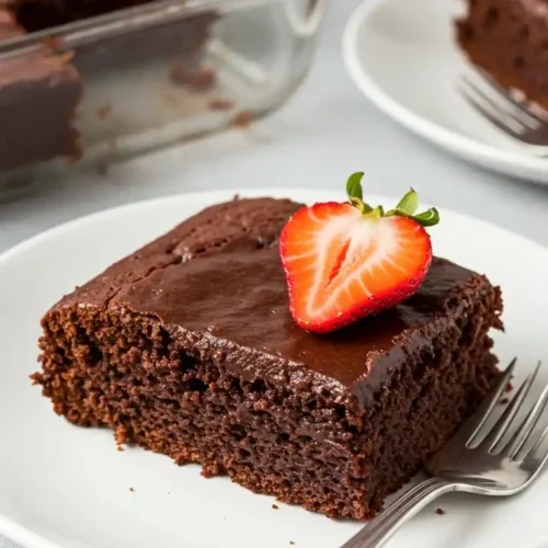 Un délicieux morceau de gâteau sans beurre au chocolat, nappé d'une ganache brillante et garni d'une fraise fraîche, prêt à être dégusté.