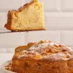 Une tranche du gâteau moelleux aux pommes de ma grand-mère est délicatement soulevée avec une spatule, révélant sa texture aérée et son parfum irrésistible, tandis que le reste du gâteau repose sur une assiette, prêt à être dégusté.