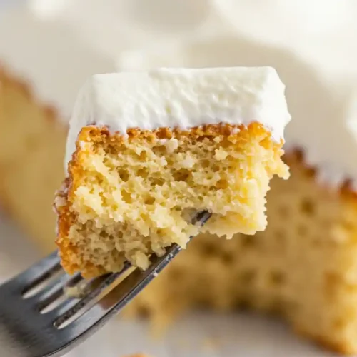 Gros plan d'une bouchée de gâteau nuage sans sucre prélevée avec une fourchette. La texture légère et aérée du gâteau est bien visible, ainsi que la couche de crème fouettée. L'arrière-plan montre le reste du gâteau et quelques miettes sur la table.