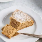 Gateau creme de marron : Une part de gâteau moelleux saupoudrée de sucre glace, présentée sur une assiette blanche avec une cuillère contenant une bouchée.