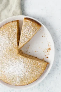 Gateau creme de marron : Vue de dessus d'un gâteau entier, saupoudré de sucre glace, avec quelques parts déjà coupées. Présentation appétissante sur une assiette blanche.