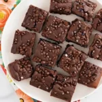 Un plateau rempli de parts de gâteau au chocolat, décorées de pépites de chocolat, présentées sur une serviette fleurie, une idée parfaite pour un gâteau goûter enfant réussi.