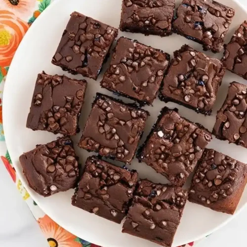 Un plateau rempli de parts de gâteau au chocolat, décorées de pépites de chocolat, présentées sur une serviette fleurie, une idée parfaite pour un gâteau goûter enfant réussi.