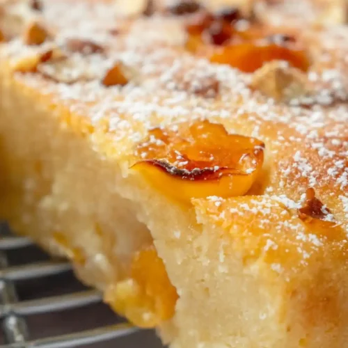Vue rapprochée d'une tranche de gâteau aux mirabelles moelleux, reposant sur une grille. On distingue clairement la texture aérée de la pâte et la douceur caramélisée des mirabelles, saupoudrées d'un léger voile de sucre glace.