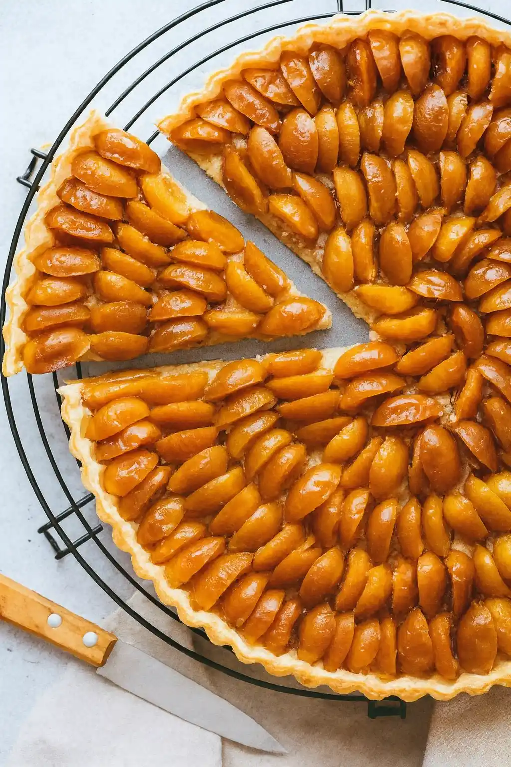 Une délicieuse tarte aux mirabelles, dont une part a été coupée, repose sur une grille. Les mirabelles sont disposées en rangées régulières et brillent grâce au glaçage. Une illustration parfaite de la tarte mirabelle recette.