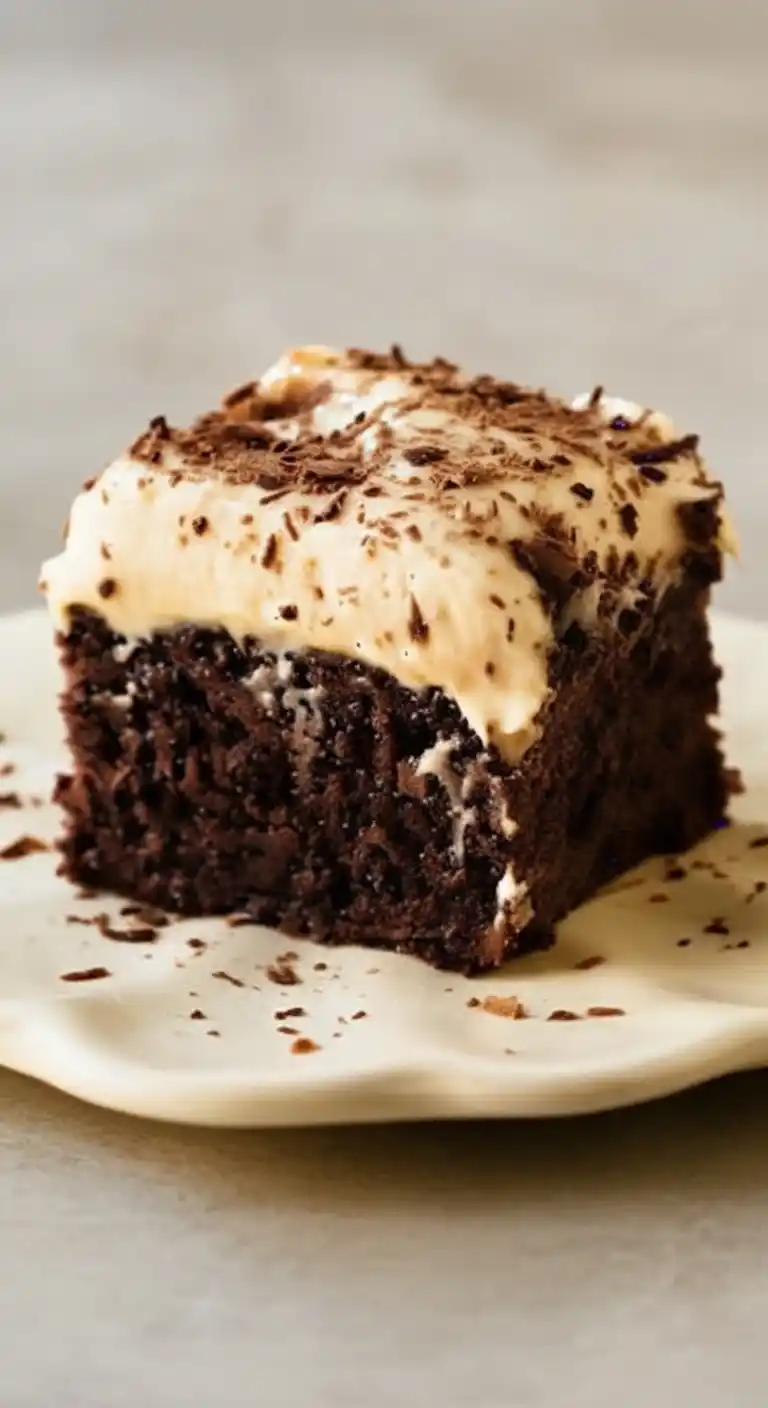Un délicieux carré de gateau au chocolat, nappé d'une crème onctueuse et décoré de copeaux de chocolat, présenté sur une assiette.