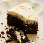 Une part appétissante de gateau au chocolat avec un glaçage crémeux, présentée sur une assiette avec des miettes éparpillées et une fourchette, prête à être dégustée.