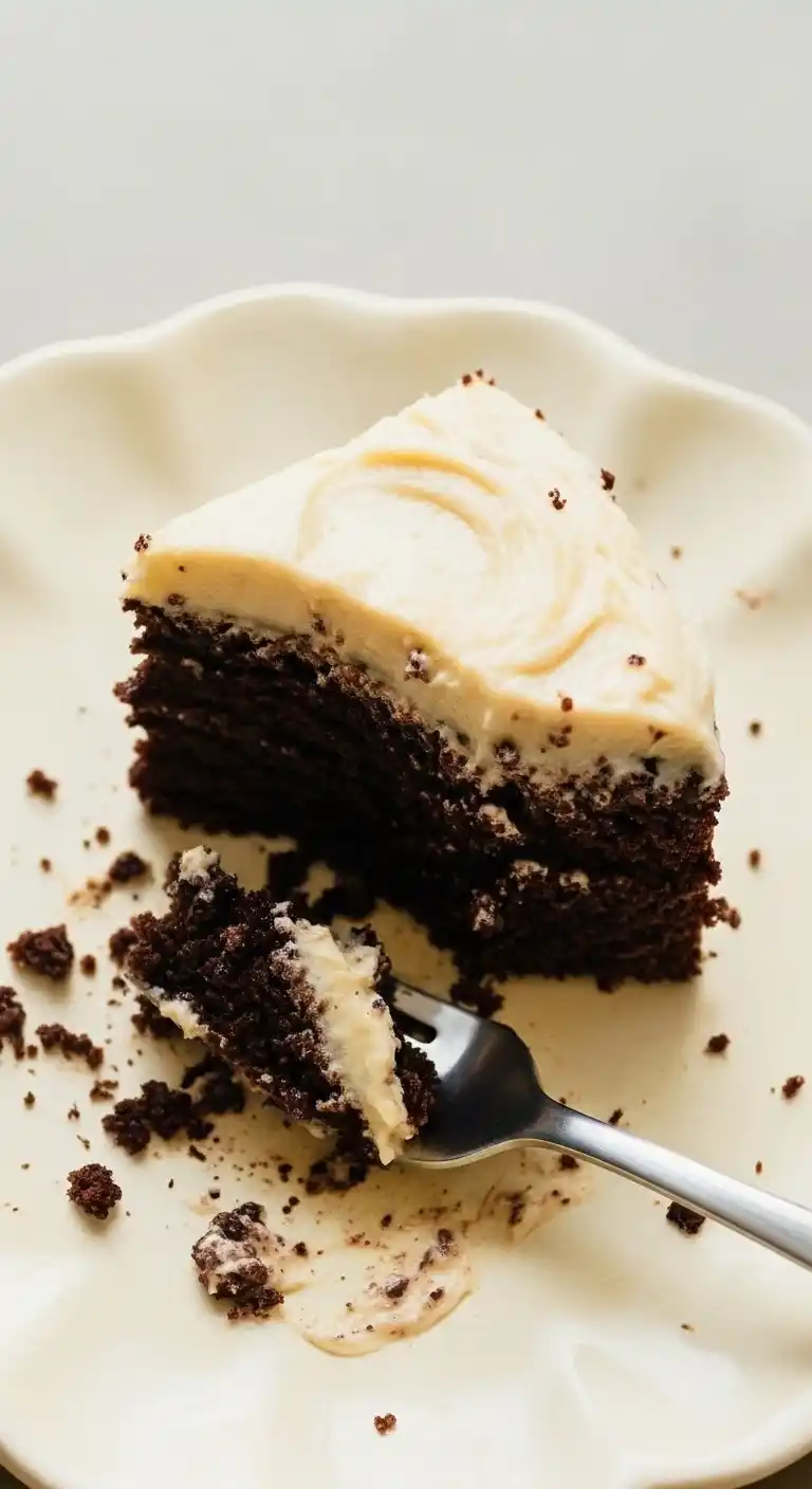 Une part appétissante de gateau au chocolat avec un glaçage crémeux, présentée sur une assiette avec des miettes éparpillées et une fourchette, prête à être dégustée.