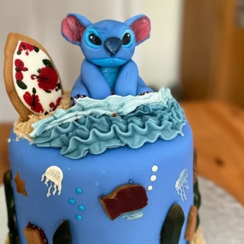 Un magnifique gâteau Stitch à plusieurs étages, décoré avec soin pour ressembler à un monde sous-marin. On y voit une figurine adorable de Stitch assis au sommet, entouré de vagues en crème fouettée, de méduses, de bulles et d'algues en sucre, pour un gâteau Stitch qui plaira à coup sûr.