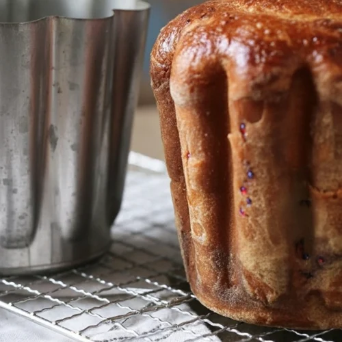 Présentation élégante d'un gateau battu traditionnel, avec sa croûte caramélisée et sa forme unique, aux côtés de son moule cannelé en métal, sur une grille à pâtisserie.