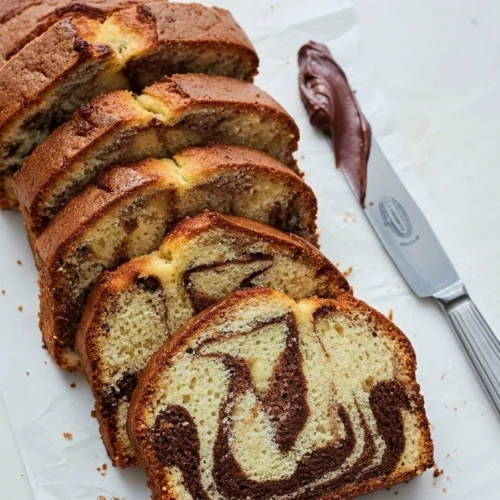 Présentation appétissante d'un savane gateau tranché, dévoilant son motif marbré chocolat-vanille, accompagné d'une spatule nappée de crème au chocolat.
