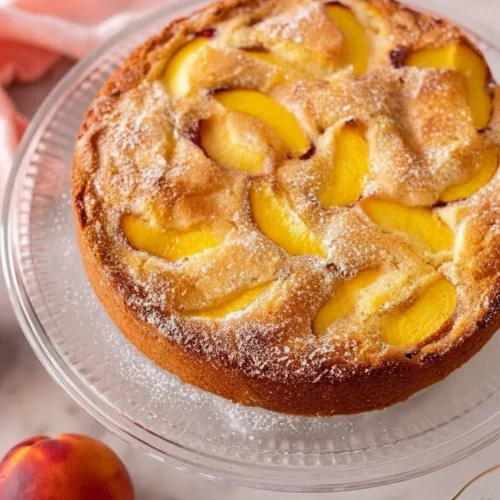 Un délicieux gateau peche fait maison, saupoudré de sucre glace, présenté sur un élégant présentoir à gâteau.