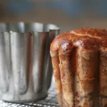 Gros plan d'un gateau battu doré et brillant, fraîchement sorti de son moule en métal cannelé, reposant sur une grille de refroidissement.
