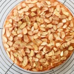 Gateau amande entier, refroidissant sur une grille après cuisson, garni d'amandes effilées.