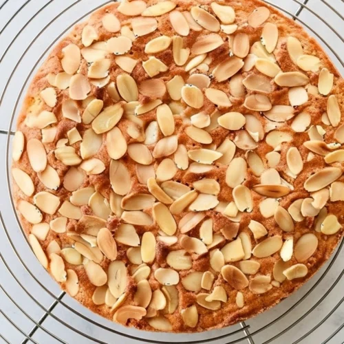 Gateau amande entier, refroidissant sur une grille après cuisson, garni d'amandes effilées.