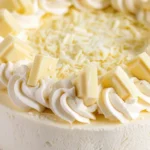 Gâteau fromage blanc décoré avec de la crème fouettée et des morceaux de chocolat blanc.