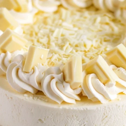 Gâteau fromage blanc décoré avec de la crème fouettée et des morceaux de chocolat blanc.