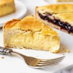 Gros plan sur une pile de parts de gâteau basque, certaines fourrées à la crème et d'autres à la cerises. La pâte dorée est bien visible et donne envie.