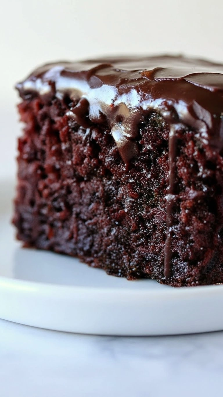 Gros plan vertical sur une part de gâteau chocolat rapide ultra moelleux, couvert d'un glaçage riche et brillant qui coule sur le bord, posé sur une assiette blanche.