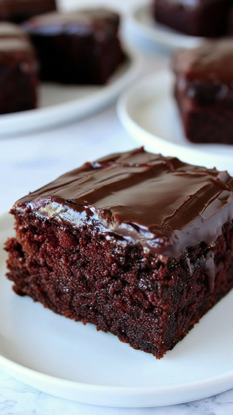 Gros plan sur une part carrée de gâteau chocolat rapide et moelleux, nappée d'un glaçage brillant qui coule sur le côté, servie sur une assiette blanche.
