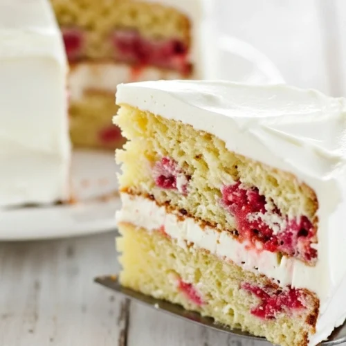 Voici une part de gâteau framboise avec deux couches de crème blanche et de framboises fraîches, posée sur une pelle à tarte.
